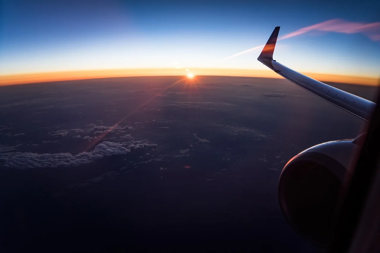View of an aeroplane wing through a cabin window above the clouds at sunset