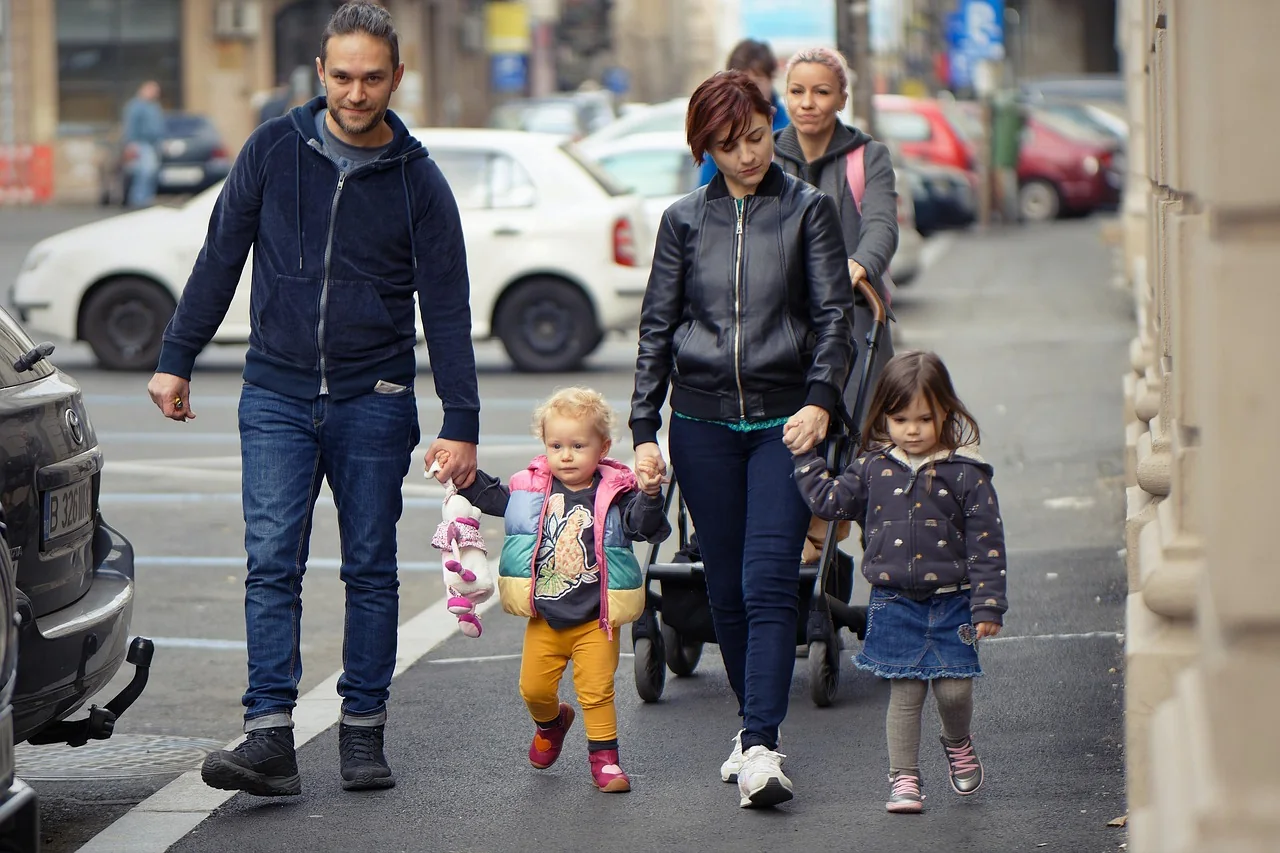 Mother and father walking hand in hand with their two young children along a sunny seafront promenade