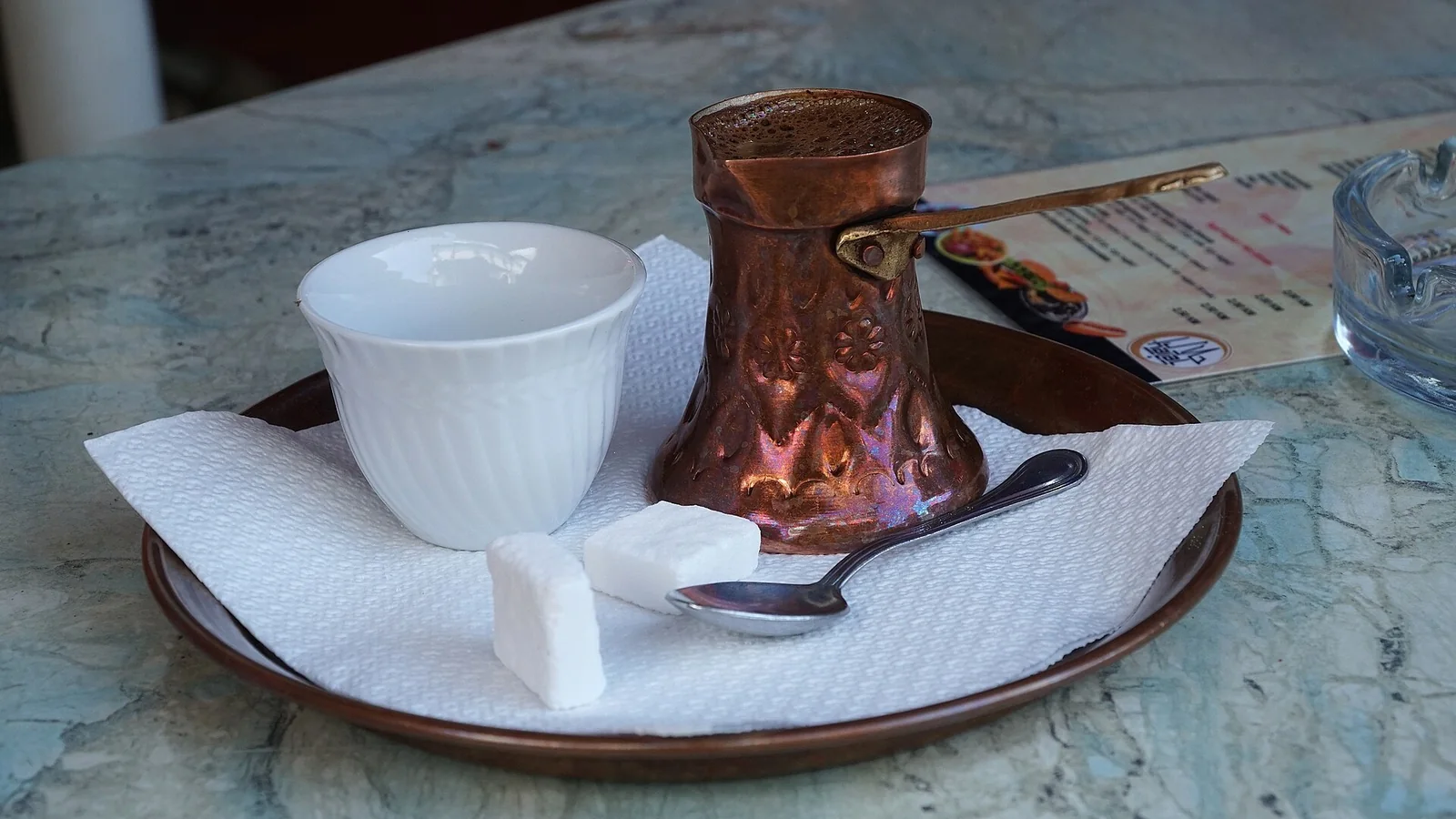 Traditional coffee served in a copper pot with a small white cup and sugar cubes