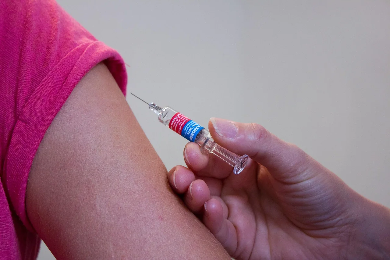 A nurse giving a seasonal flu vaccine injection in the upper arm of an older woman at a doctor's clinic