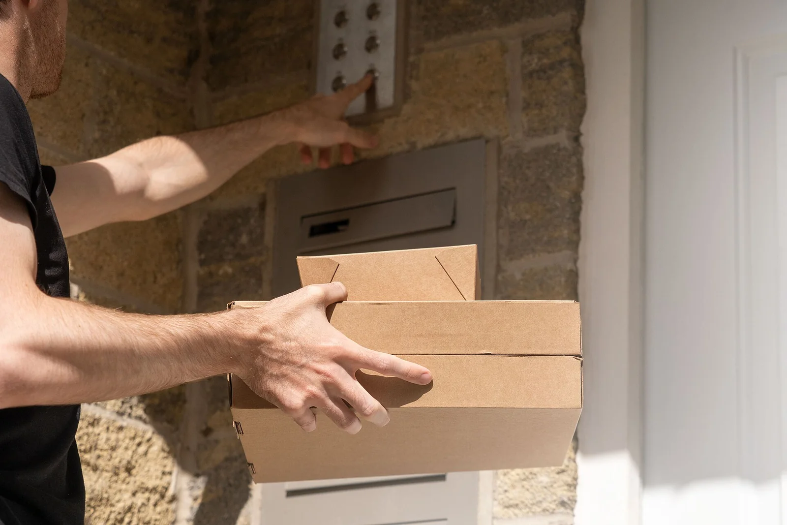 Courier ringing an apartment doorbell while holding two cardboard takeaway boxes