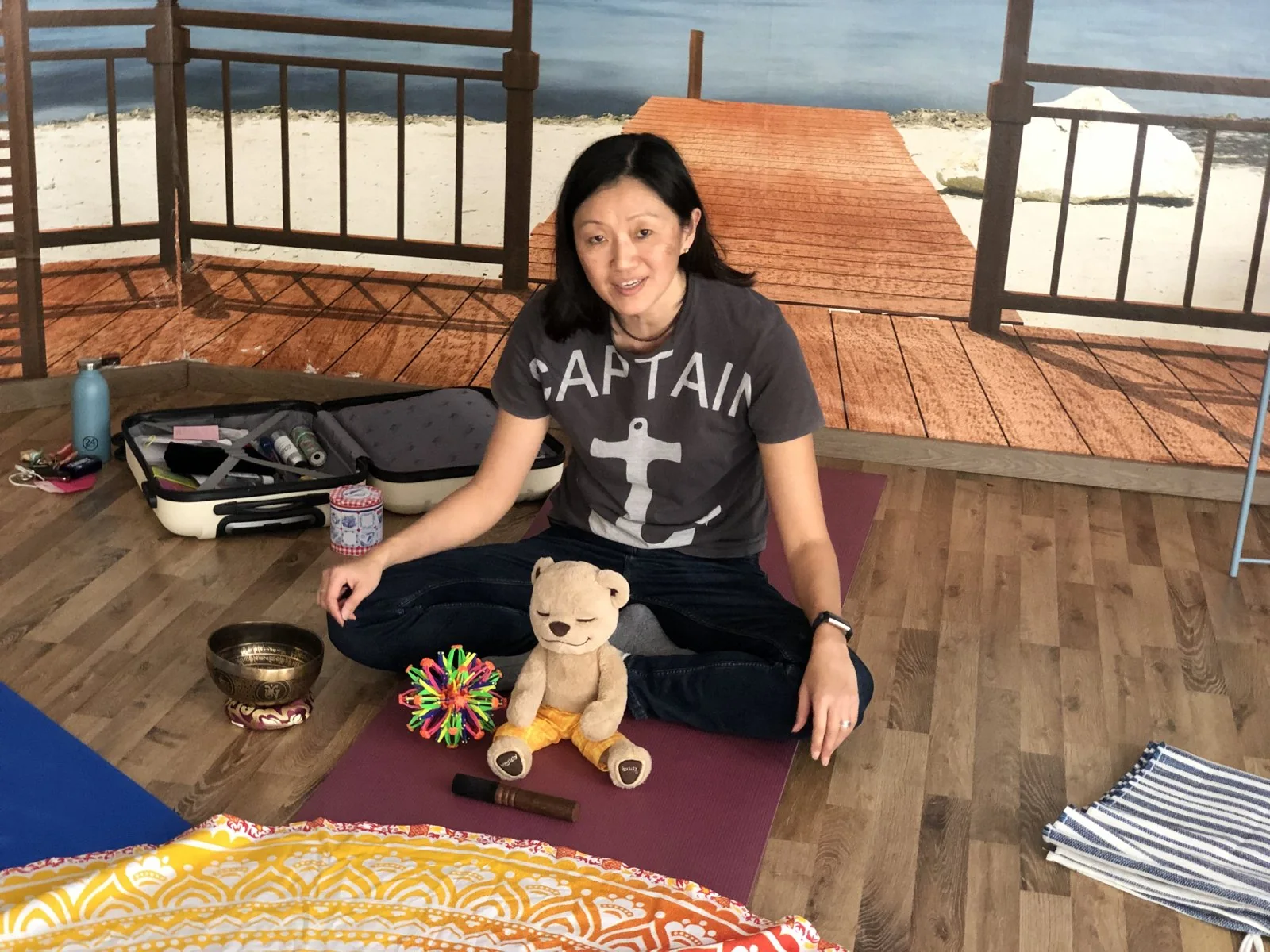 Judy Lam sitting on a meditation mat with a singing bowl and a teddy bear, ready for a children's mindfulness session