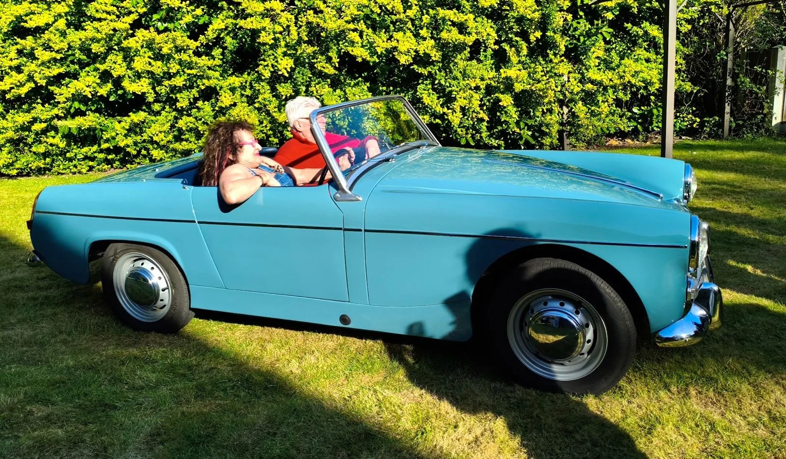 Michael and Sarah, a British couple planning to retire to Cyprus, sitting in a pale blue classic convertible on a sunny lawn