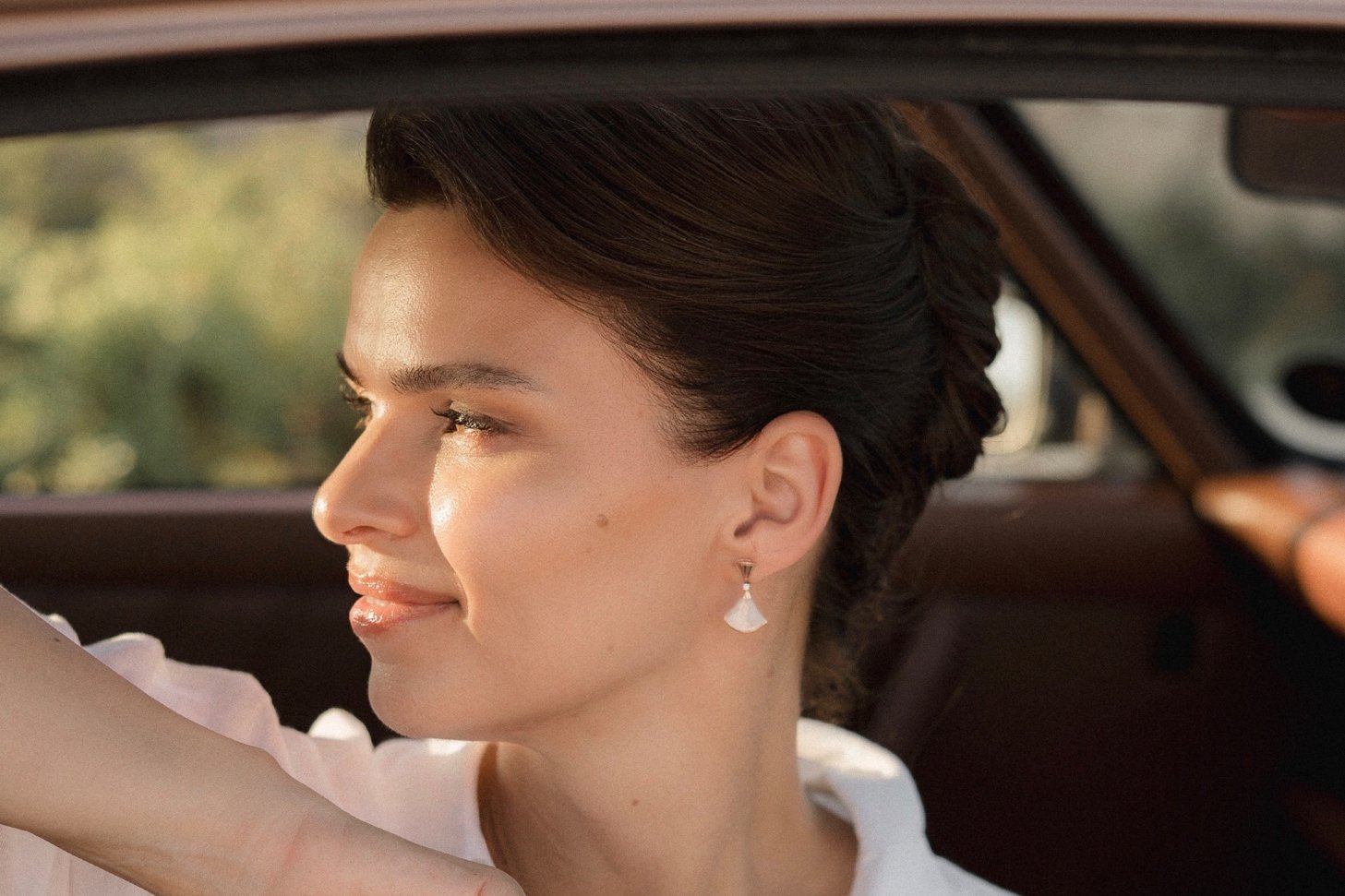 Simona in a vintage car, holding the KAMÈ Enhancing Brow Serum