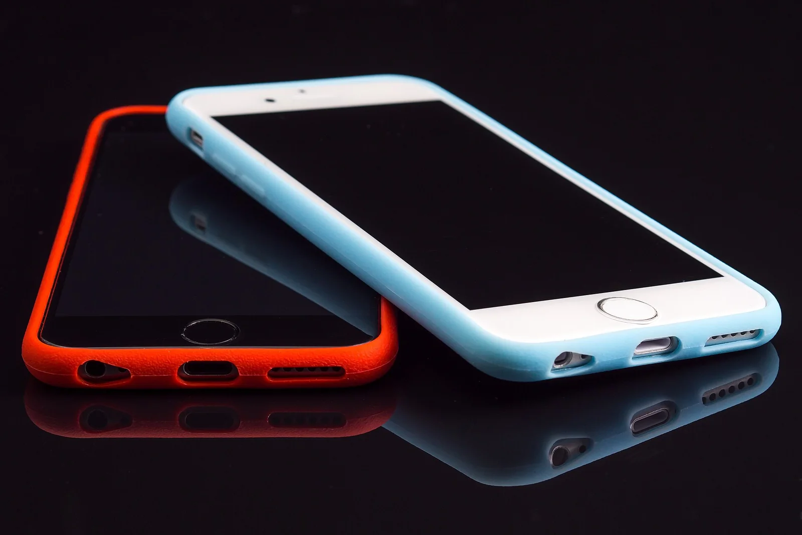 Two smartphones lying on a dark reflective surface