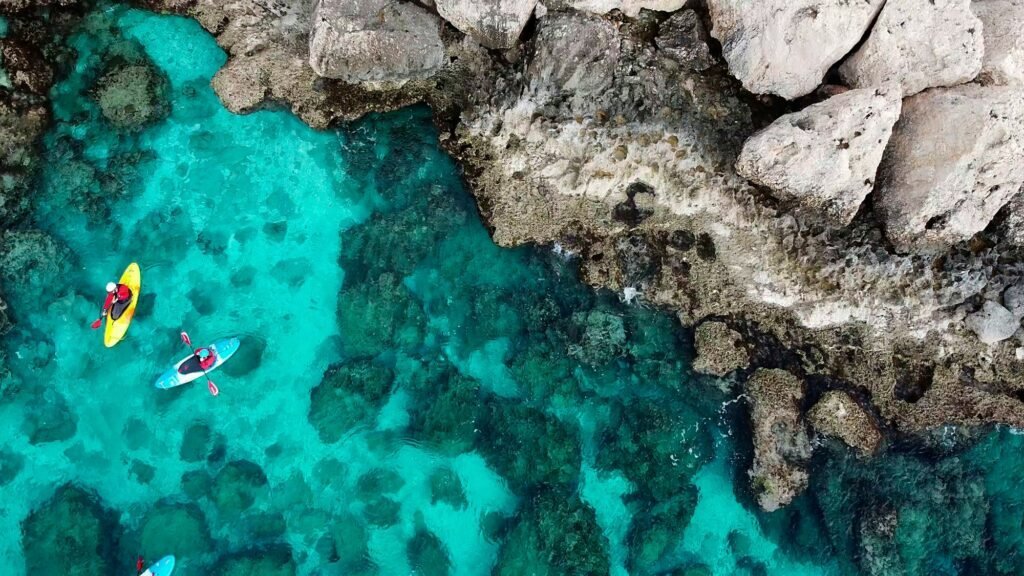 People kayaking in the sea near mountains and a sea cave, seen from a drone